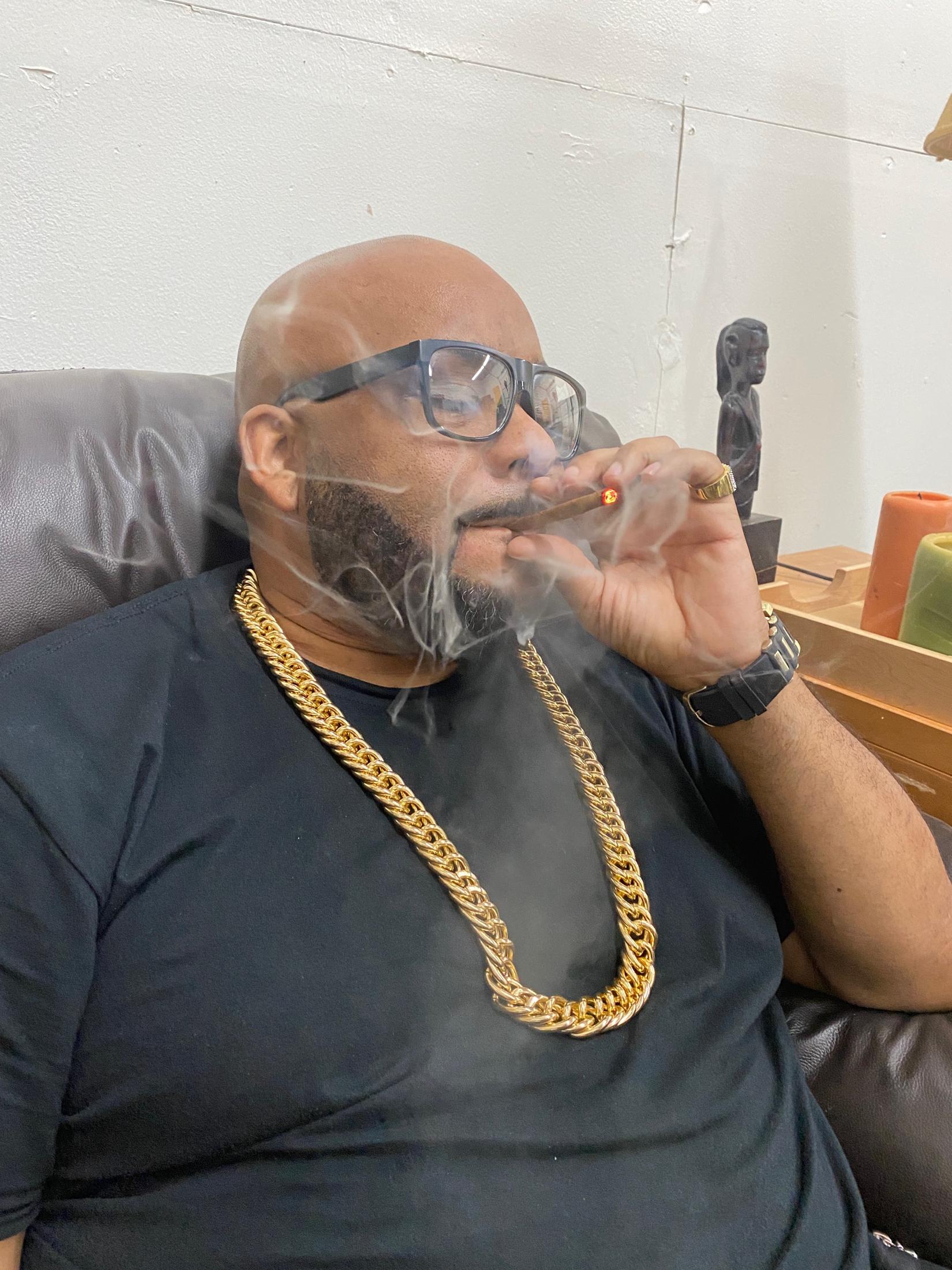 Boogie Taylor seated in a warm studio lounge, holding a cigar